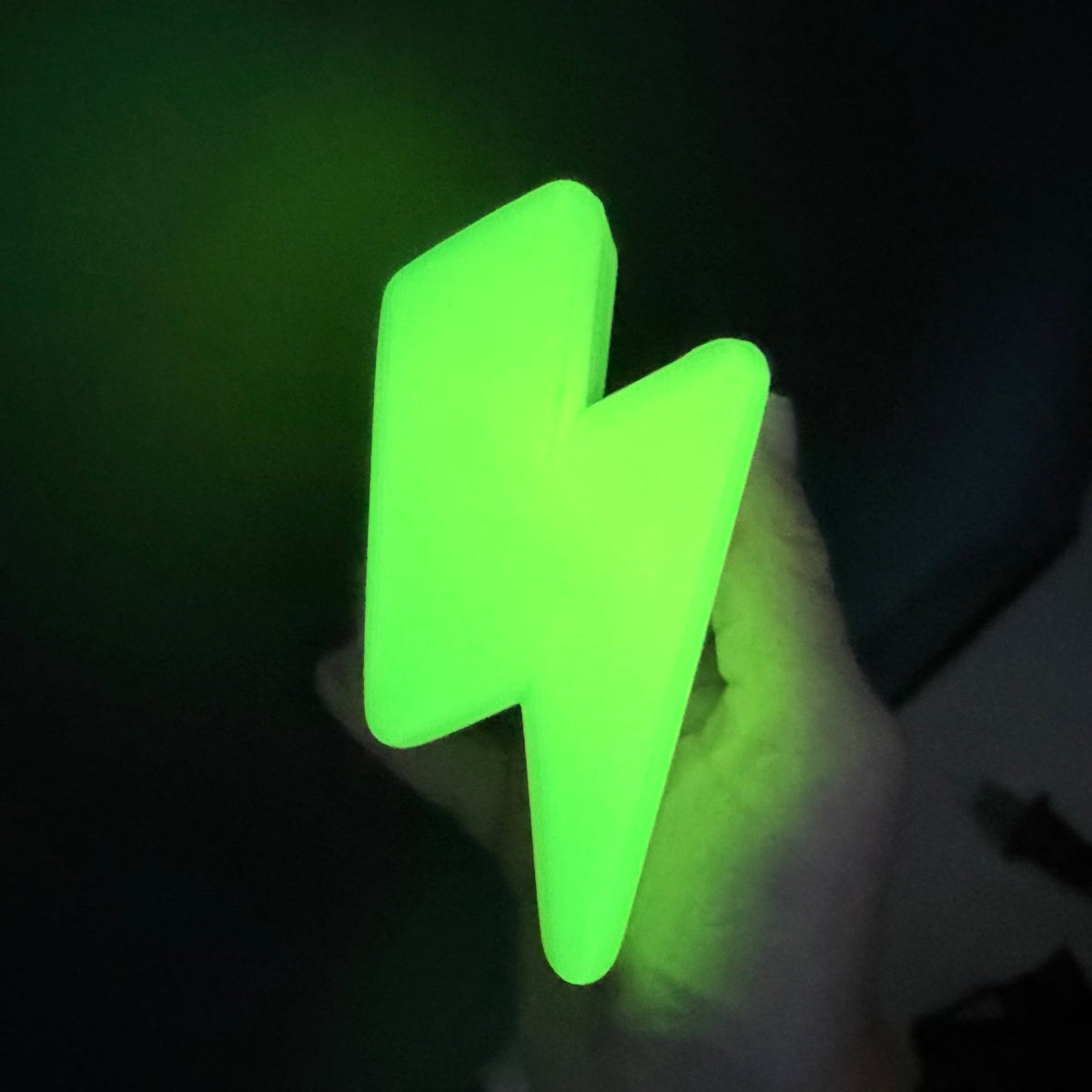 A hand holding a glowing green lightning bolt-shaped night light against a dark background.